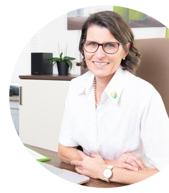 Eine Frau (Ariane Zappe) lächelnd am Schreibtisch in ihrer Praxis.